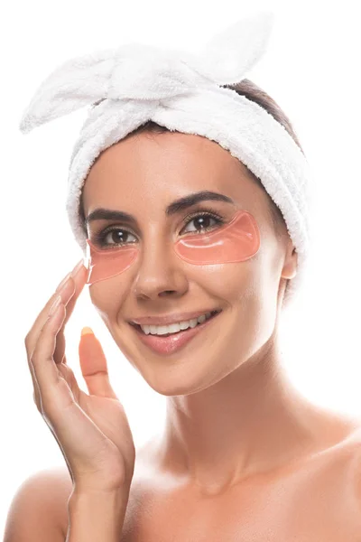 Jeune femme nue en bande capillaire cosmétique avec des bandeaux oculaires souriant isolé sur blanc — Photo de stock