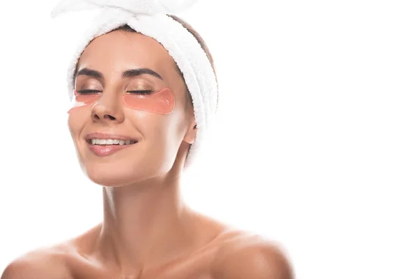Nude young woman in cosmetic hair band with eye patches smiling with closed eyes isolated on white — Stock Photo