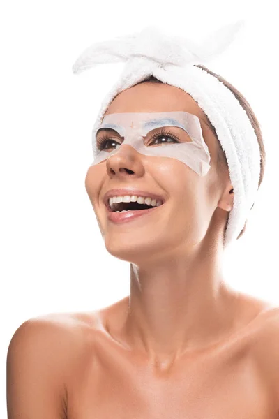 Mujer joven desnuda en banda de pelo cosmético con máscara facial riendo aislado en blanco - foto de stock