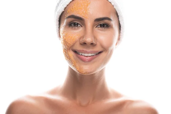 Vue de face de jeune femme souriante en bande capillaire cosmétique avec gommage sur le visage isolé sur blanc — Photo de stock