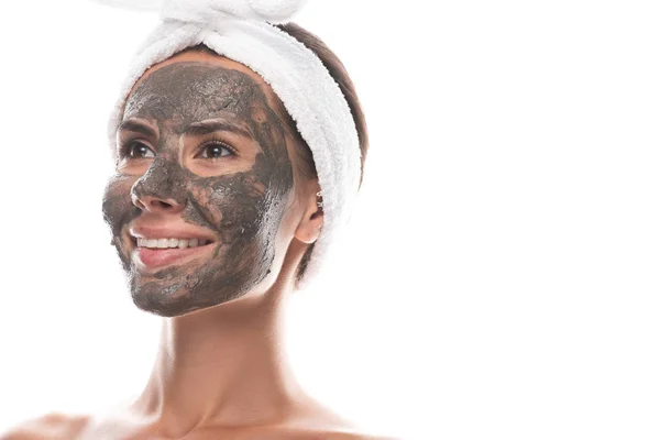 Nudo giovane donna in fascia di capelli cosmetici con maschera di argilla sul viso sorridente e guardando lontano isolato su bianco — Foto stock