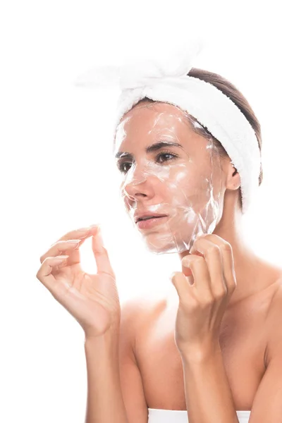 Mujer joven en banda de pelo cosmético con máscara facial aislado en blanco - foto de stock
