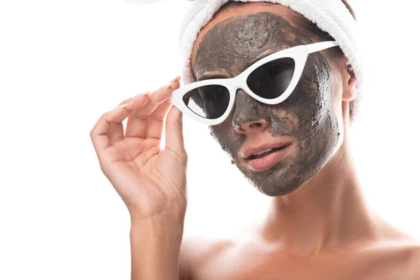 Mujer joven desnuda en banda de pelo cosmético y gafas de sol con máscara de arcilla en la cara aislada en blanco - foto de stock