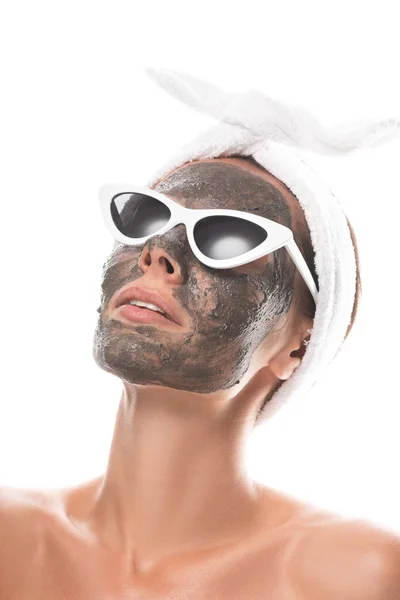 Nackte junge Frau in kosmetischem Haarband und Sonnenbrille mit Tonmaske auf dem Gesicht isoliert auf weiß — Stockfoto