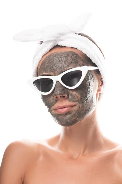 Nackte junge Frau in kosmetischem Haarband und Sonnenbrille mit Tonmaske auf dem Gesicht isoliert auf weiß — Stockfoto