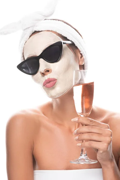 Femme en lunettes de soleil et bande capillaire cosmétique avec masque facial tenant verre à vin isolé sur blanc — Photo de stock
