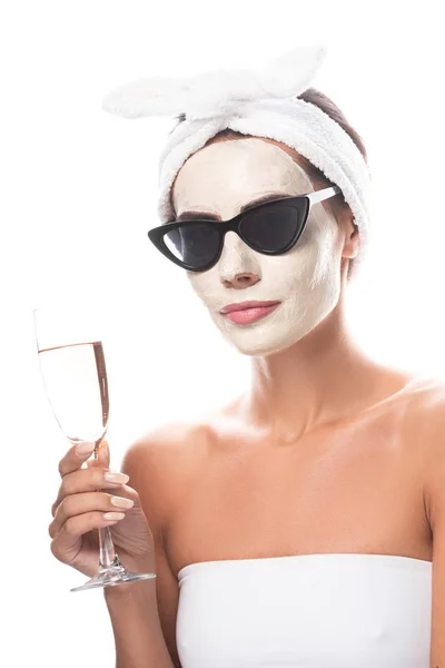 Woman in sunglasses and cosmetic hair band with facial mask holding wine glass isolated on white — Stock Photo