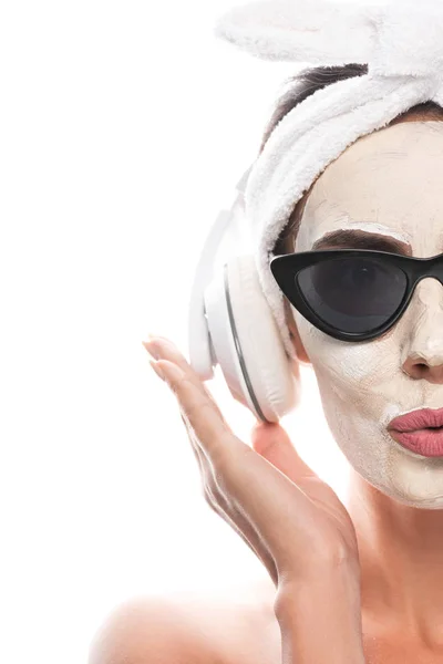 Cropped view of nude woman in cosmetic hair band and sunglasses with facial mask listening music in headphones isolated on white — Stock Photo