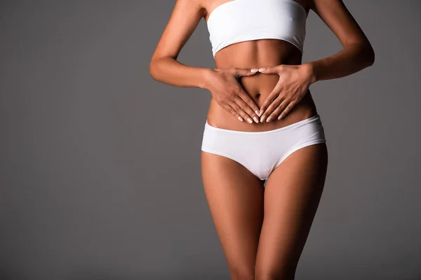 Abgeschnittene Ansicht einer sexy jungen Frau in Unterwäsche, die den Bauch berührt, isoliert auf grau — Stockfoto