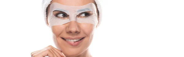 Plano panorámico de mujer sonriente en banda de pelo cosmético con máscara facial aislado en blanco - foto de stock