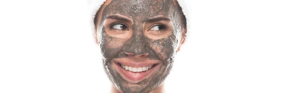 Panoramaaufnahme einer lächelnden Frau mit Tonmaske auf dem Gesicht, die isoliert auf Weiß wegschaut — Stockfoto