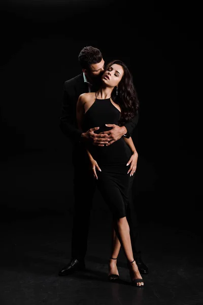 Man hugging woman with closed eyes standing in dress on black — Stock Photo