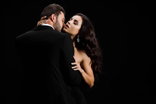 Passionate man in suit kissing attractive woman isolated on black — Stock Photo