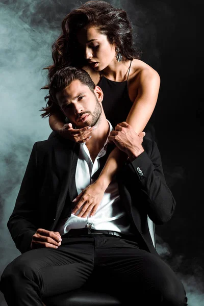 Leidenschaftliches Mädchen steht und umarmt gutaussehenden bärtigen Mann auf schwarz mit Rauch — Stockfoto