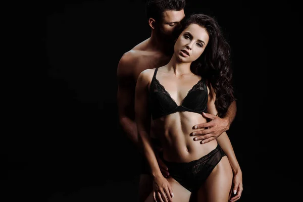 Чоловік обіймає сексуальну жінку в мереживній білизні ізольовано на чорному — стокове фото