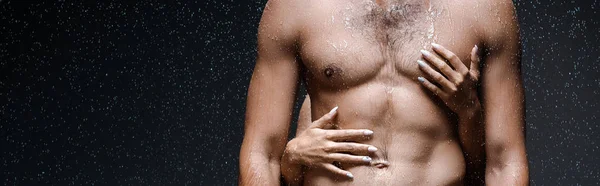 Colpo panoramico di ragazza abbracciando sexy uomo senza maglietta sotto gocce di pioggia sul nero — Foto stock