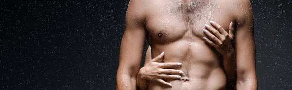 Panoramic shot of girl hugging sexy shirtless man under raindrops on black — Stock Photo