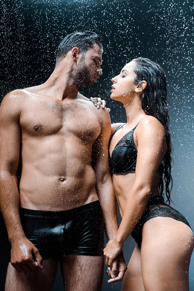 Mojado sin camisa hombre de pie con novia bajo gotas de lluvia en negro - foto de stock