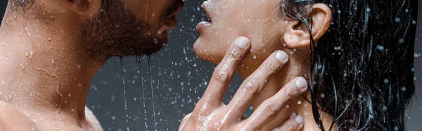 Panoramic shot of wet man touching face of girlfriend under raindrops on black — Stock Photo