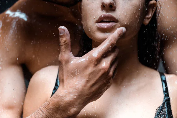 Abgeschnittene Ansicht eines Mannes, der das Gesicht seiner Freundin unter Regentropfen auf Schwarz berührt — Stockfoto