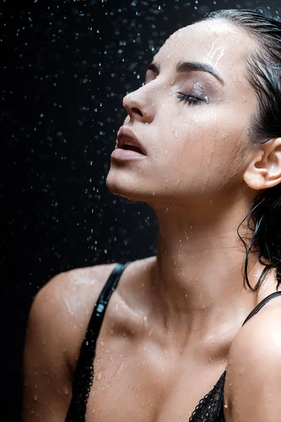 Jovem atraente com olhos fechados sob gotas de chuva em preto — Fotografia de Stock