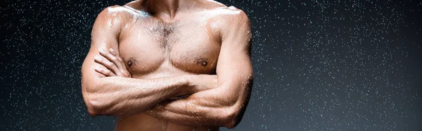 Панорамний знімок мокрого чоловіка, що стоїть з схрещеними руками під краплями на чорному — стокове фото