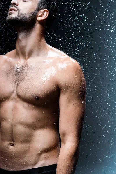 Vue recadrée de homme sexy torse nu debout sous les gouttes de pluie sur noir — Photo de stock