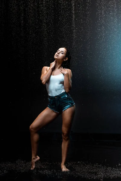 Sexy junge und nasse Frau steht unter Regentropfen auf schwarz — Stockfoto