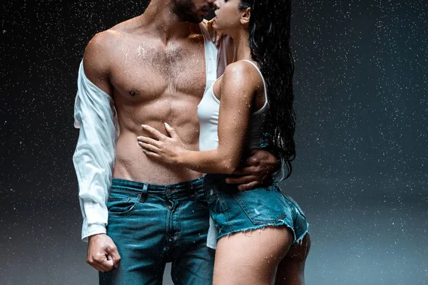 Corte vista de despido muscular homem de pé com sexy menina sob gotas de chuva no preto — Fotografia de Stock