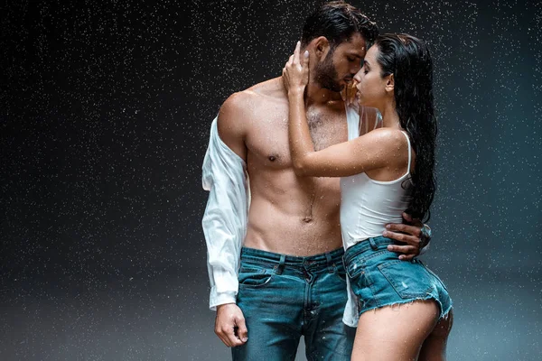 Homem despido e musculoso de pé com menina sexy sob gotas de chuva em preto — Fotografia de Stock