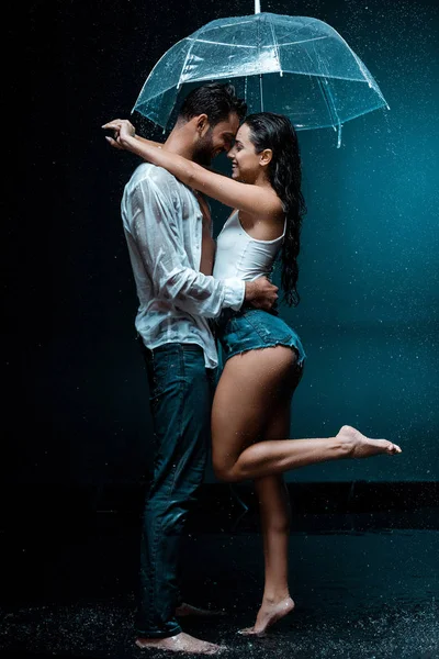 Side view of happy girl standing with handsome man and umbrella on black — Stock Photo