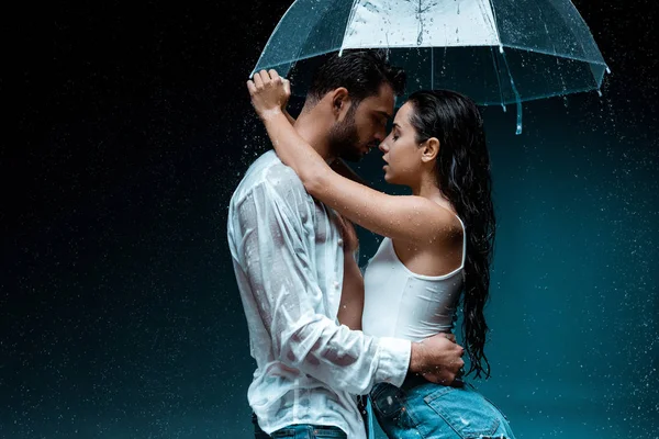 Side view of attractive girlfriend hugging handsome boyfriend and holding umbrella on black — Stock Photo