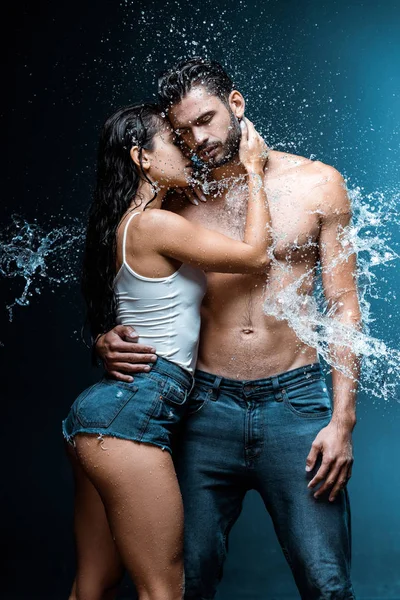 Sexy and wet woman hugging handsome and muscular boyfriend under raindrops on black — Stock Photo