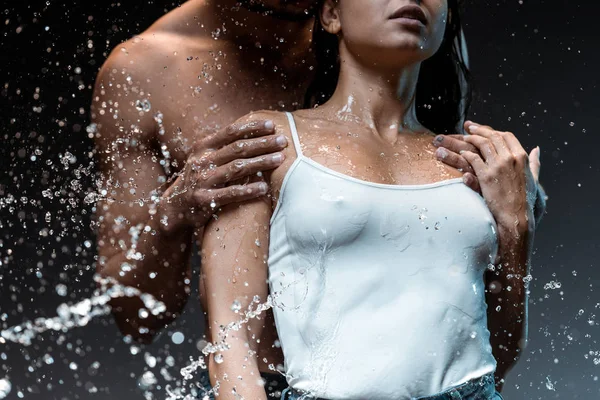 Selective focus of man hugging sexy woman near splash of water on black — Stock Photo