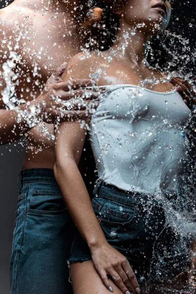 Corte vista de homem sem camisa despir namorada perto respingo de água no preto — Fotografia de Stock