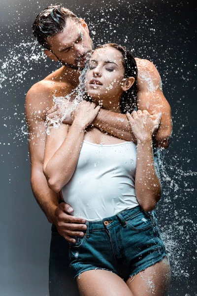 Uomo bello e senza maglietta abbracciando bella fidanzata vicino spruzzata d'acqua sul nero — Foto stock