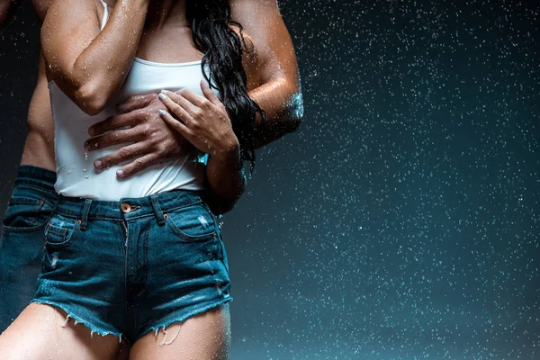 Cropped view of man hugging wet girl in denim shorts on black — Stock Photo