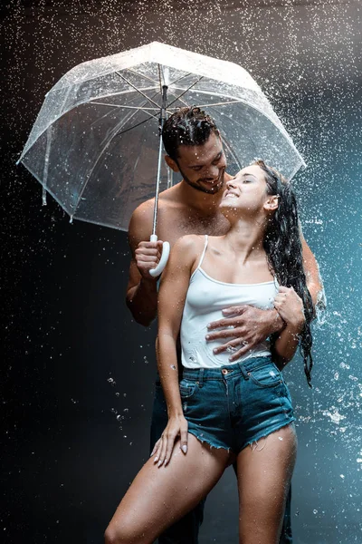 Felice uomo barbuto abbracciando allegra fidanzata e tenendo ombrello su nero — Foto stock