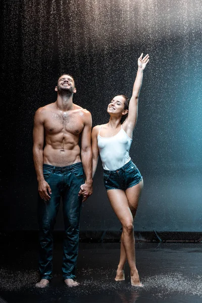 Feliz casal de pé e de mãos dadas sob gotas de chuva em preto — Fotografia de Stock