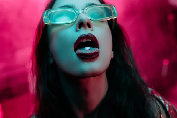 Beautiful girl in sunglasses with lsd on tongue in nightclub — Stock Photo