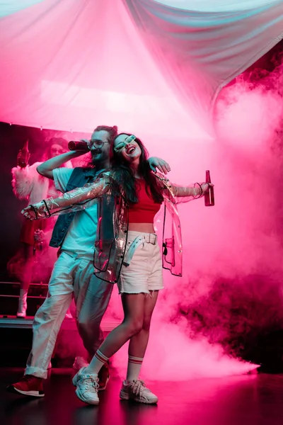 Hombre feliz y hermosa chica bailando en discoteca con humo rosa - foto de stock