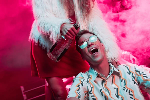Chica con alcohol cerca de hombre en gafas de sol con lsd en la lengua en discoteca - foto de stock