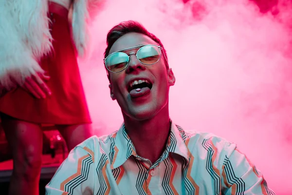 Man in sunglasses with lsd on tongue in nightclub with pink smoke — Stock Photo