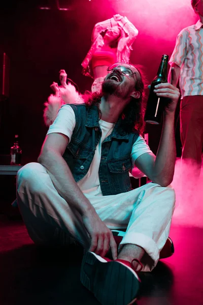Felice uomo in occhiali da sole con bottiglia di alcol durante il rave in discoteca — Foto stock