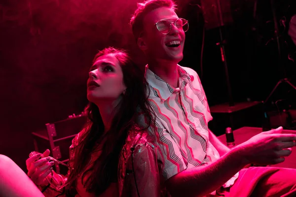 Uomo e giovane donna seduti insieme durante la festa rave in discoteca — Stock Photo