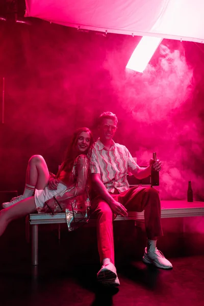 Улыбающийся мужчина с пивом сидит рядом с девушкой в ночном клубе во время рейва — стоковое фото