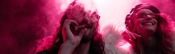 Panoramic shot of man smoking marijuana joint near smiling girl in nightclub — Stock Photo