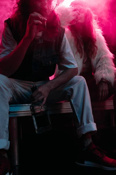 Homme avec de l'alcool fumer cigarette près de la jeune femme pendant la fête rave dans la boîte de nuit — Photo de stock