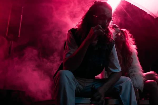 Homme fumant la cigarette près de la jeune femme pendant la fête rave dans la boîte de nuit — Photo de stock