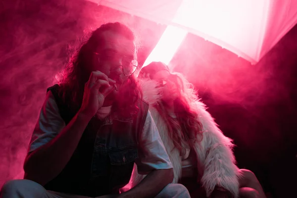 Man smoking cigarette near young woman during rave party in nightclub — Stock Photo